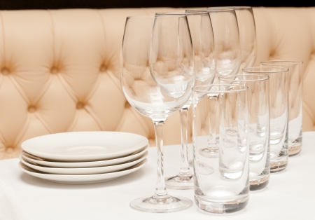 White table with glasses and plates with a leather divan on background. Focus on front glass.の写真素材