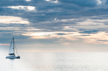 Sailing yacht in sunset on tranquil sea and cloudy skyの写真素材