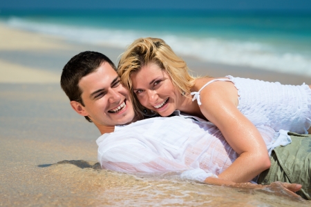 Happy embracing young couple lie on sand of a tropical beach with blue sea on backgroundの写真素材