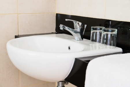 Ceramic hand wash basin in a hotel with chrome water mixer tap, white towel and two glassesの写真素材