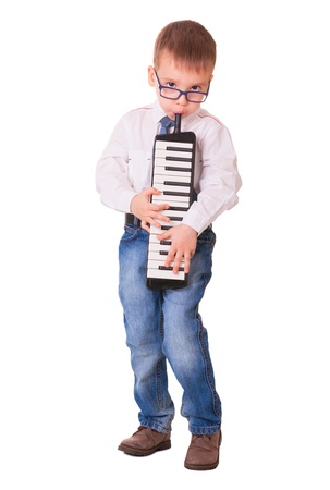 Preschool boy in glasses, jeans and white shirt playing melodica, isolated on white backgroundの写真素材
