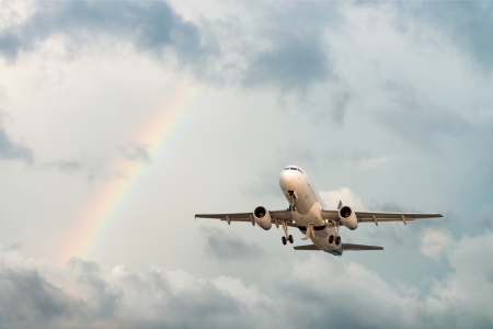 Airplane flying in cloudy sky with rainbow after rainの写真素材