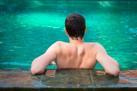 Back view of young men relaxing in a swimming pool on a poolside in tropical resortの写真素材