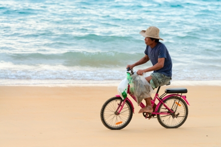 PHUKET, THAILAND - FEB 15: Old native local man bicycling along a sand beach on Feb 28, 2013 in Phuket, Thailand. Small law bicycles are common among Thailanders のeditorial素材