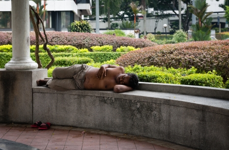KUALA LUMPUR - JUN 15: Homeless men sleeping on a bench in a public park on a midday on Jun 15, 2013 in Kuala Lumpur, Malaysia. Homeless people in KL often take over parks for restingのeditorial素材