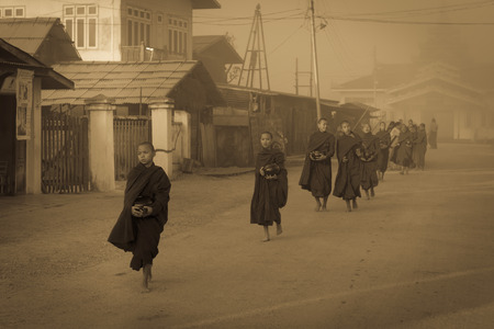 INLE LAKE, MYANMAR - 08 JAN 2014: Young monks gather food on early morning almsround. Offering food is one of the oldest and most common rituals in Buddhism.のeditorial素材