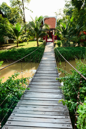 Wooden long rope bridge cross the stream in green tropical parkの写真素材