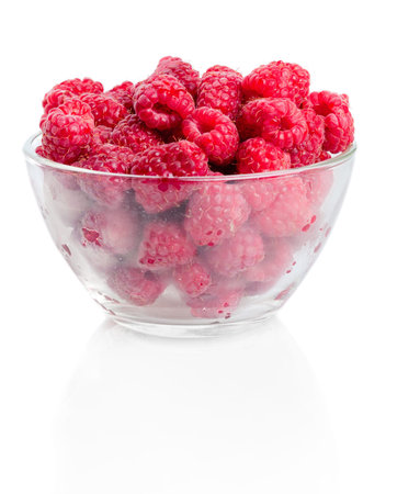 Fresh picked ripe red organic raspberries in glass bowl on white background