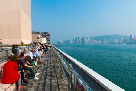 HONG KONG CHINA  18 JAN 2015:  Tourists and visitors sit and wait on benches along Kowloon Promenade with a beautiful unobstructed view of Hong Kong's skyline in the background.のeditorial素材