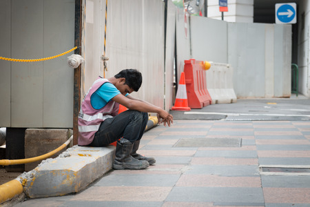 SINGAPORE - 21 DEC 2013: Exhausted construction worker sits on a cement slab at a project worksite in Singapore to take a break.のeditorial素材