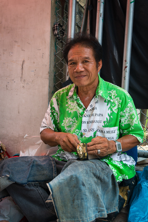 BANGKOK, THAILAND - 07 MAY 2014: A traditional street shoemaker, smiling sitting against a wire fence.のeditorial素材