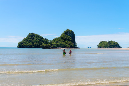 KRABI, THAILAND - 13 OCT 2014: Tourists couple walking in shallow water with tropical islands and sand beach in the background and clear blue sky at Ao Nangのeditorial素材