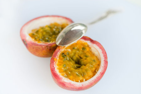 Silver spoon with its bowl resting on the center of a halved passion fruit, with its sticky insides and many small seeds.の写真素材