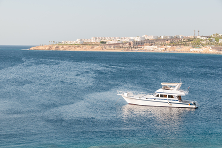 Small, white yacht with stainless steel railings, anchored in the warm waters of a tropical bay on a sunny day.の写真素材