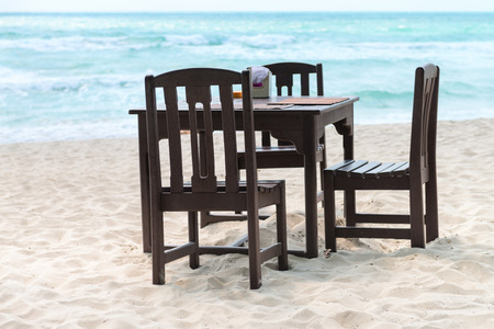 Wooden table and chairs in romantic cafe standing on the tropical sand beach near the sea