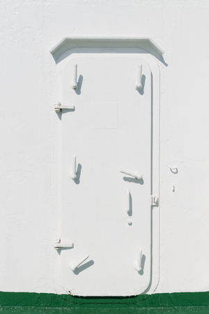Narrow closed iron door with many locks on a ship painted in white colorの写真素材