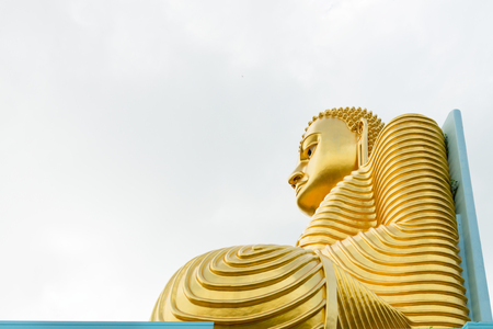 Big golden Buddha statue in sitting pose on the top of a building with cloudy white sky on backgroundの写真素材