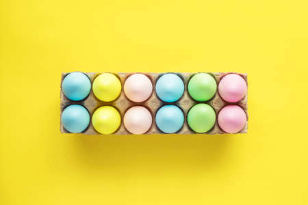 Easter colored eggs in box on yellow background.