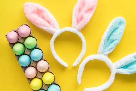 Easter holiday flat lay on yellow background. Colored Easter eggs and bunny headbands for children. Egg hunting concept.の写真素材