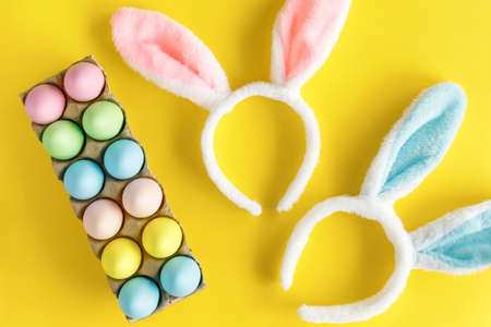 Easter holiday flat lay on yellow background. Colored Easter eggs and bunny headbands for children. Egg hunting concept.の写真素材
