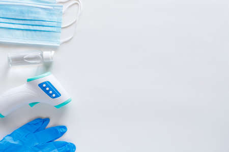 virus protection concept flat lay. Non-contact infrared body thermometer, latex gloves, disposable masks and sanitizer on white background with copy space.の写真素材