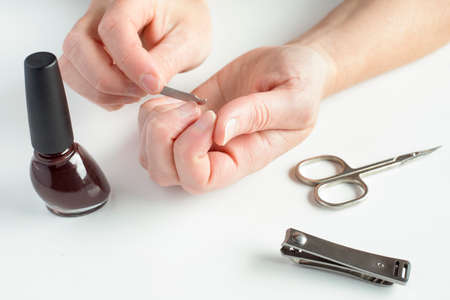 Woman hands doing manicure. Female hands, holding nail file, with nail polish, scissors and nail clippers on white background.の写真素材