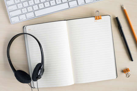 Business work top table mock up with blank notebook for text in the middle. Working or studying concept. Flat lay on desk with computer keyboard, headphones, notepad and stationery.の写真素材