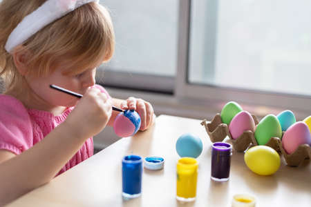 Little girl in Easter bunny ears painting colored eggs. Easter family holiday celebration at home and craft concept.の写真素材