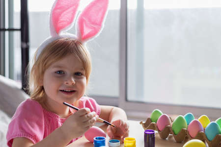 Little girl in Easter bunny ears painting colored eggs. Easter family holiday celebration at home and craft concept.の写真素材