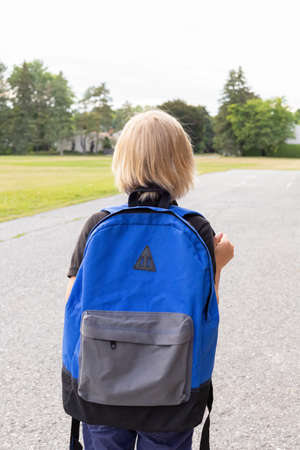 Little blond child carrying blue backpack, walking to school. Back to school concept. Child near...