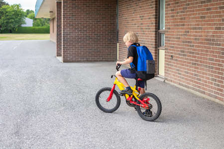 Little child going to school on a bicycle. Student riding bike near school building.