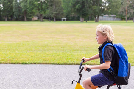 Little child going to school on a bicycle. Student with bike at schoolyard. School soccer field and a boy riding a bike.の写真素材