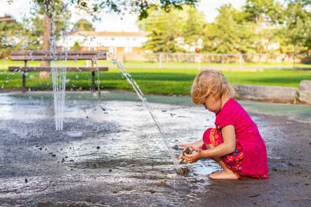 Little girl playing with splash pad water and dirt in the park on sunny day in summer.の写真素材
