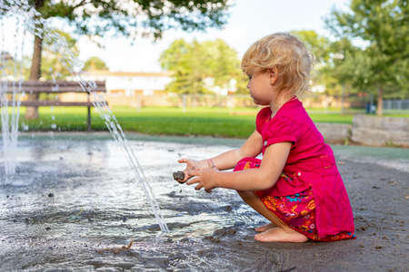 Little girl playing with splash pad water and dirt in the park on sunny day in summer.の写真素材