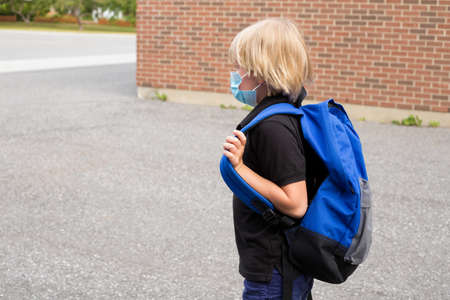 Little kid wearing mask and carrying backpack, going to school.の写真素材
