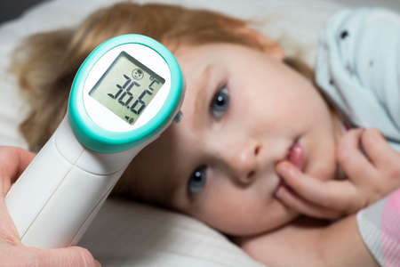 Taking temperature of a little child, lying in bed. A parent measures temperature of his kid with...