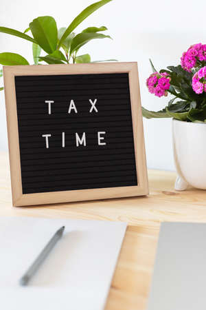 Tax time black felt letter board, laptop, notebook and flower pots on the table. Business tax return concept.の写真素材