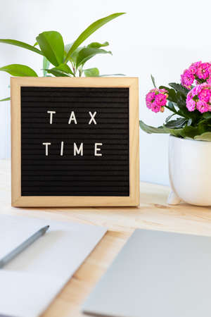 Tax time black felt letter board, laptop, notebook and flower pots on the table. Business tax return concept.の写真素材