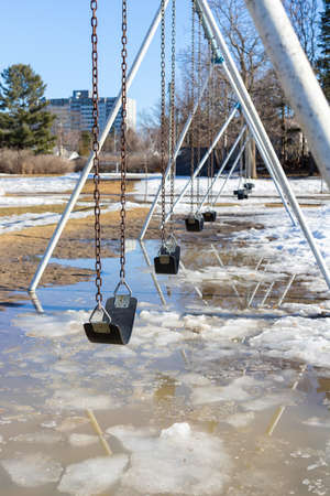Early spring in the park with swings at the playground and dirty melting snow on the ground. Flooding during springtime.の写真素材