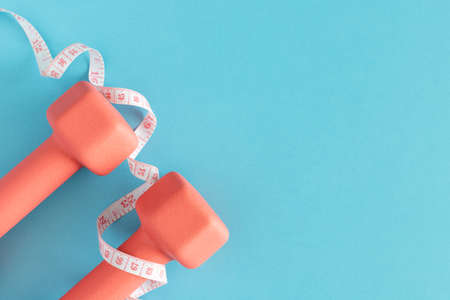 Dumbbells and measuring tape on blue background. Fitness, sport and workout concept flat lay. Weights layout with copy spaceの写真素材