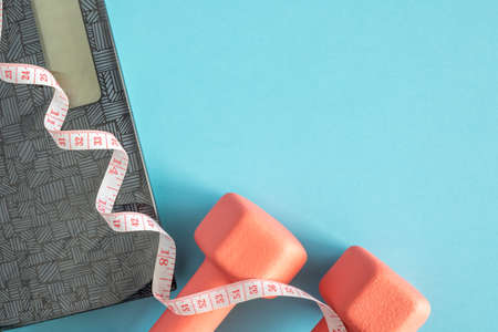 Dumbbells, scales and measuring tape on blue background. Fitness, sport and workout concept flat lay. Weights layout with copy spaceの写真素材