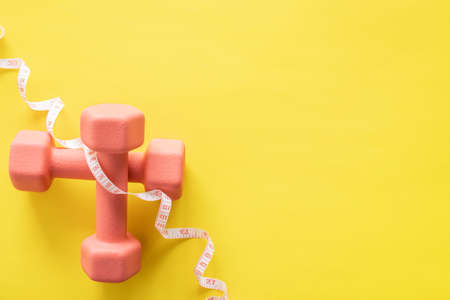 Dumbbells and measuring tape on yellow background. Fitness, sport and workout concept flat lay. Weights layout with copy space.の写真素材