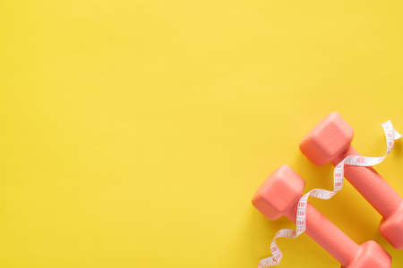 Dumbbells and measuring tape on yellow background. Fitness, sport and workout concept flat lay. Weights layout with copy space.の写真素材
