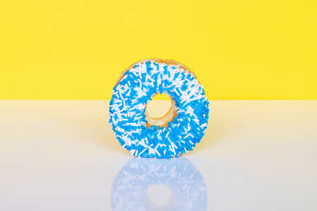 Donut with blue and white sprinkles on yellow background with reflection and copy space for text.の写真素材