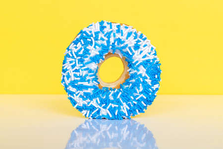Donut with blue and white sprinkles on yellow background with reflection and copy space for text.の写真素材