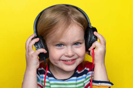 Happy smiling little child listening to music with large headphones, isolated on yellow background.の写真素材