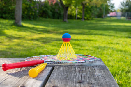 Badminton game rackets and shuttlecock on wooden table with green grass backgroud in the park on a sunny summer day. Active lifestyle concept. Fun outdoors leisure activities for a family.の写真素材