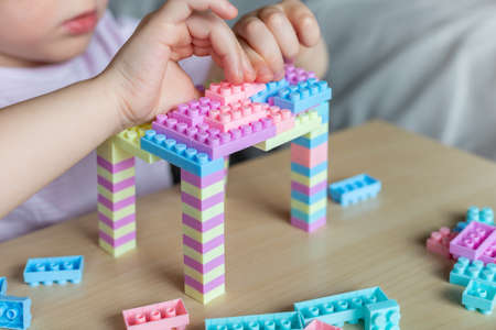 Little beautiful child playing with toy plastic building blocks, sitting at the table. Small girl busy with fun creative leisure activity. Development of fine motor skills for children.の写真素材