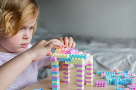 Little beautiful child playing with toy plastic building blocks, sitting at the table. Small girl busy with fun creative leisure activity. Development of fine motor skills for children.の写真素材