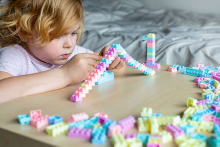 Little beautiful child playing with toy plastic building blocks, sitting at the table. Small girl busy with fun creative leisure activity. Development of fine motor skills for children.の写真素材
